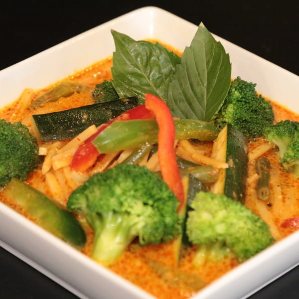 Charm Thai Cuisine's red curry with broccoli, zucchini, bell peppers, and bamboo shoots, garnished with basil.