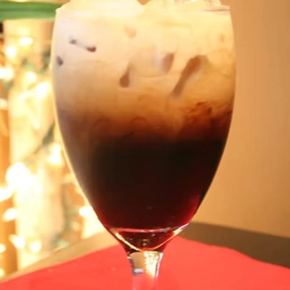 A tall glass of Thai iced tea with dark tea at the bottom and creamy milk on top.