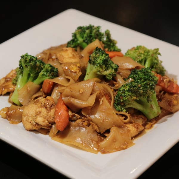 Charm Thai Cuisine's Pad See Ew with wide noodles, chicken, broccoli, and carrots on a white plate.