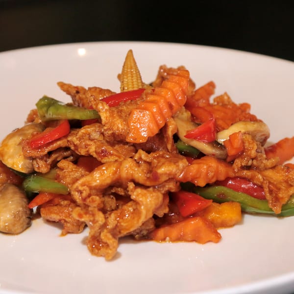Sweet and sour chicken with bell peppers, carrots, and baby corn on a white plate.