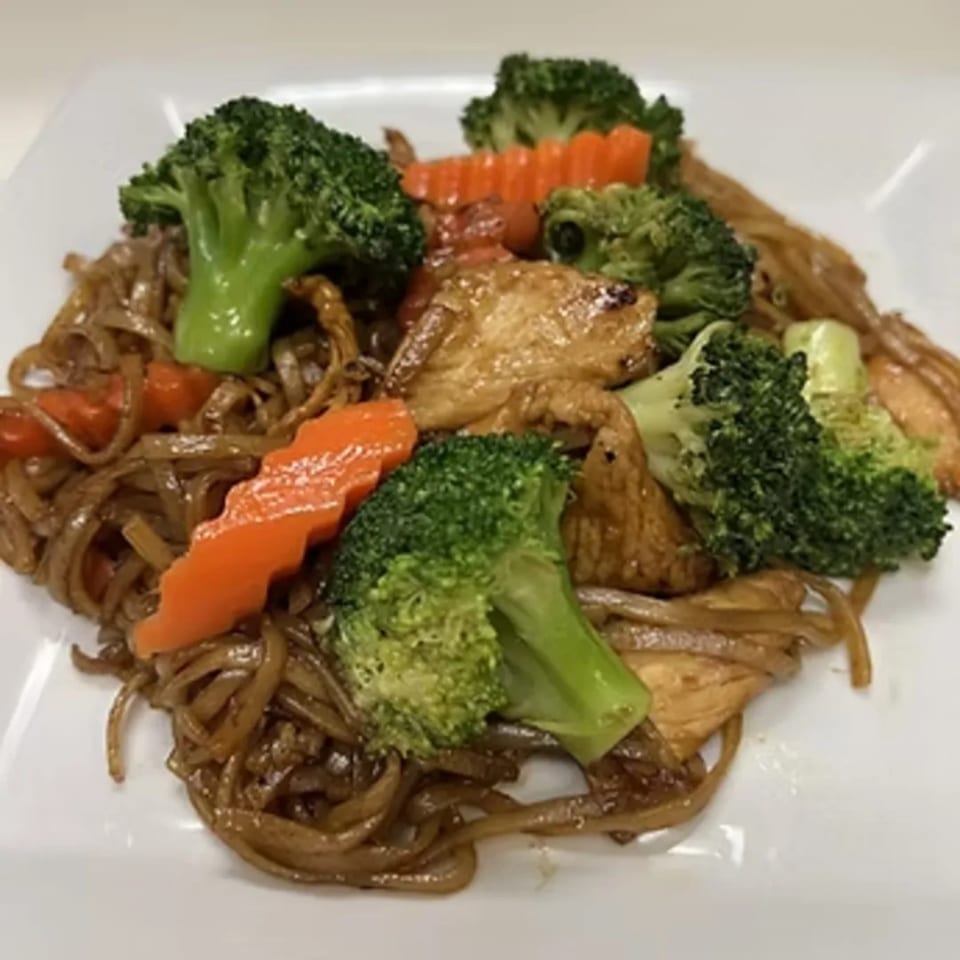 Charm Thai Cuisine's stir-fried noodles with chicken, broccoli, and carrots on a white plate.
