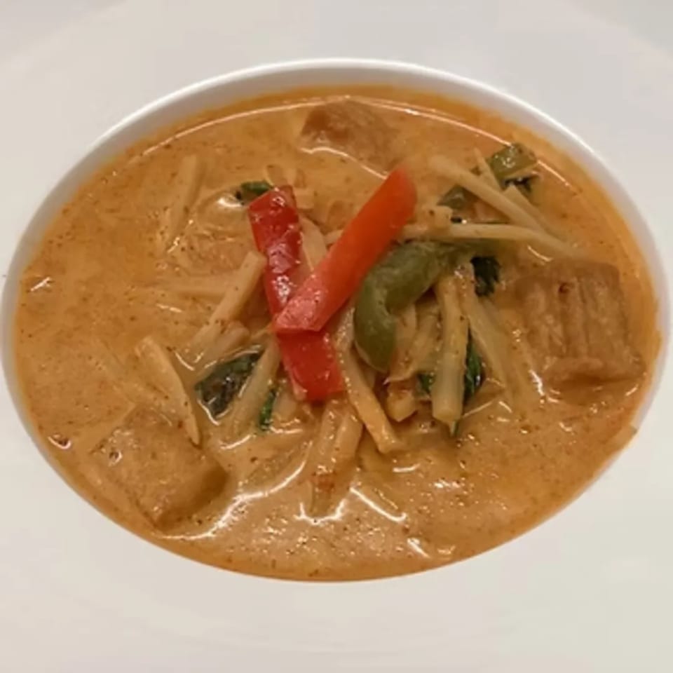 Charm Thai Cuisine's red curry with bamboo shoots, bell peppers, and chicken in a white bowl.