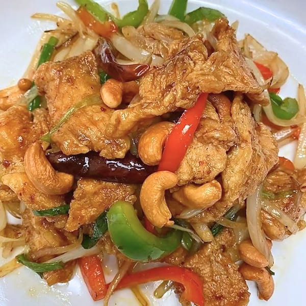 Charm Thai Cuisine's stir-fried chicken with cashews, bell peppers, and onions on a white plate.