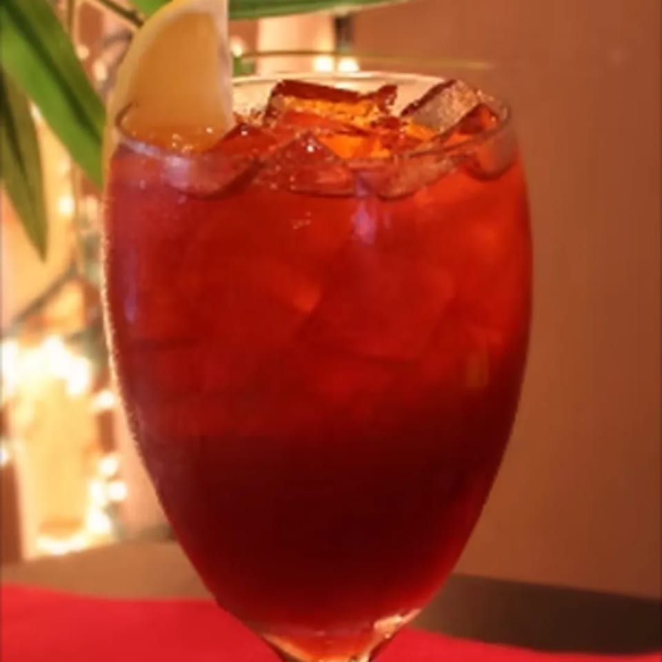 A tall glass of iced Thai tea, garnished with a lemon slice, on a red tablecloth.