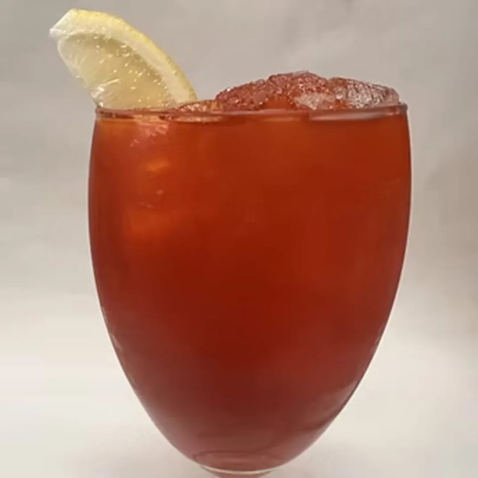 A vibrant red Thai iced tea with crushed ice and a lemon slice on a white background.