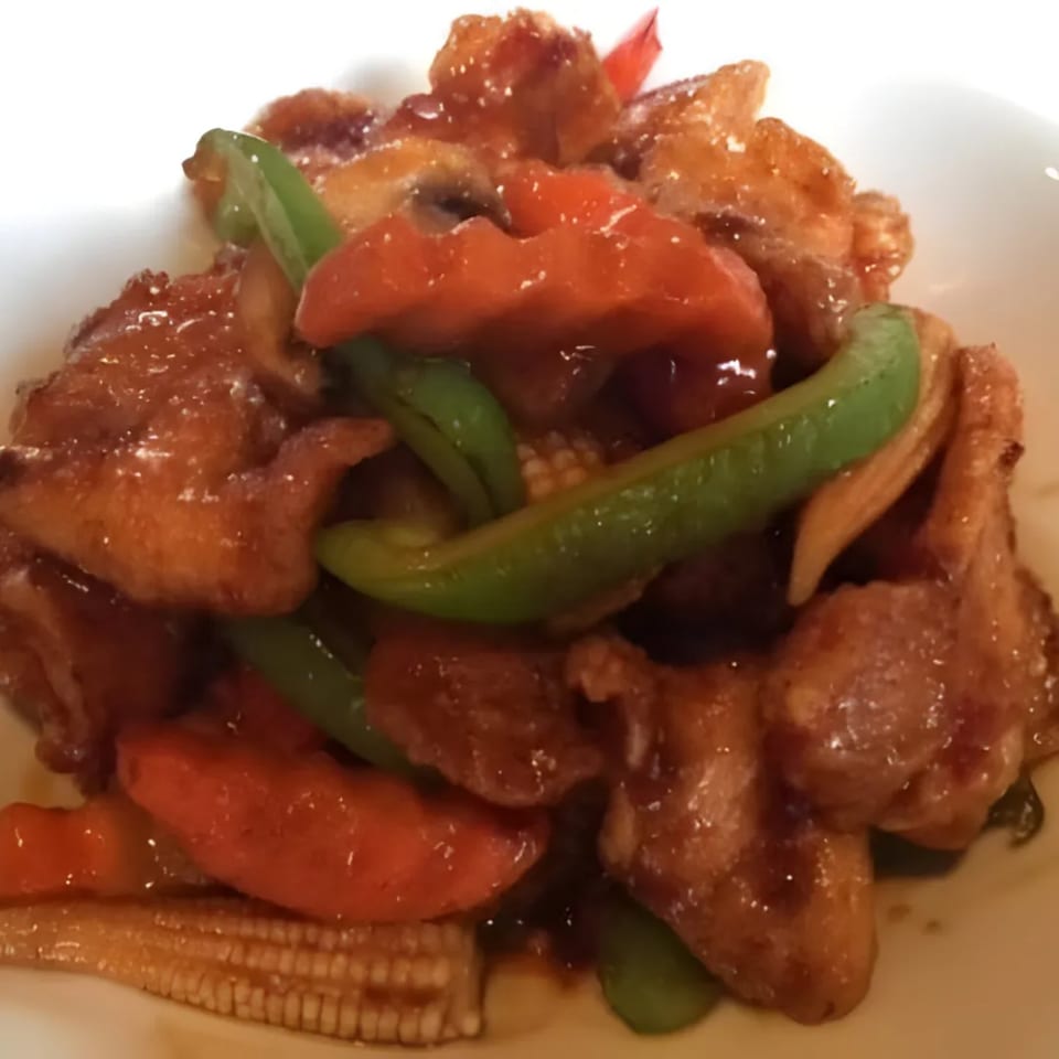 Sweet and sour chicken with red peppers, green beans, and baby corn on a white plate.