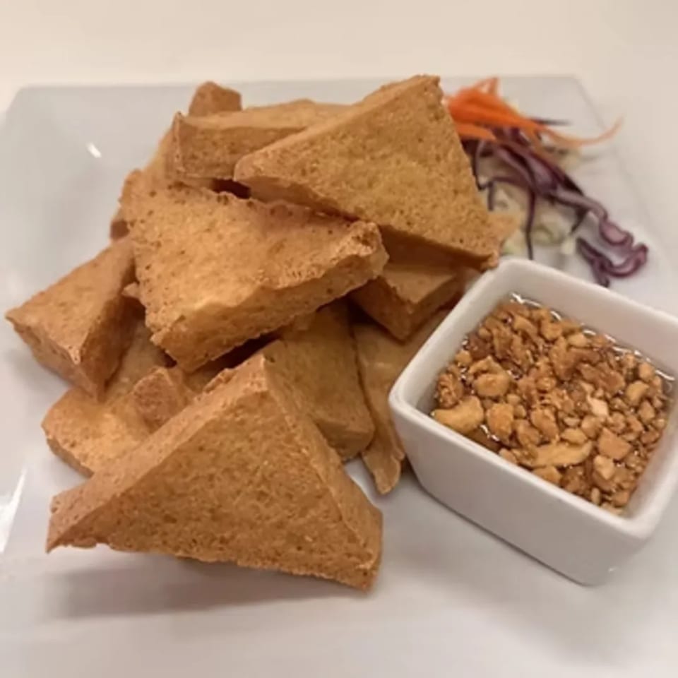 A plate of golden-brown fried tofu triangles with a side of dipping sauce topped with crushed peanuts.