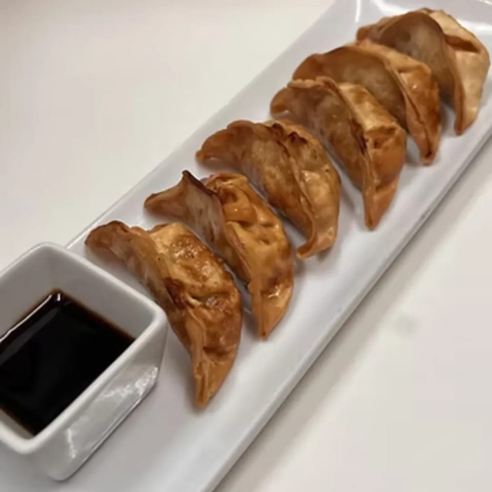 Seven crispy fried dumplings on a white rectangular plate with a side of dark dipping sauce.