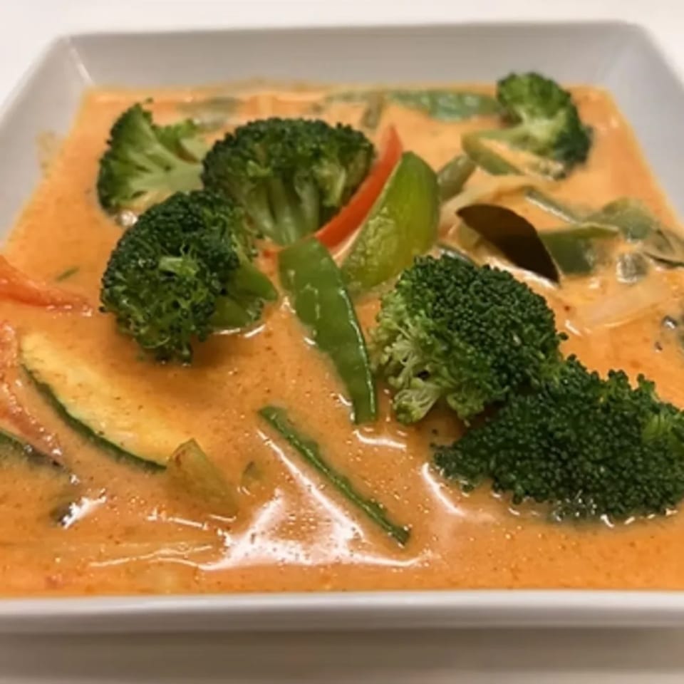 Charm Thai Cuisine's red curry with broccoli, zucchini, bell peppers, and snap peas in a white bowl.