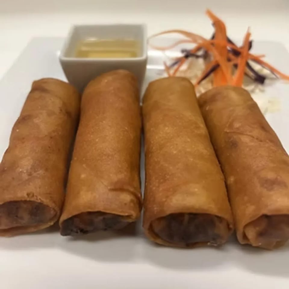 Four golden-brown Charm Thai Cuisine spring rolls with dipping sauce and shredded garnish.
