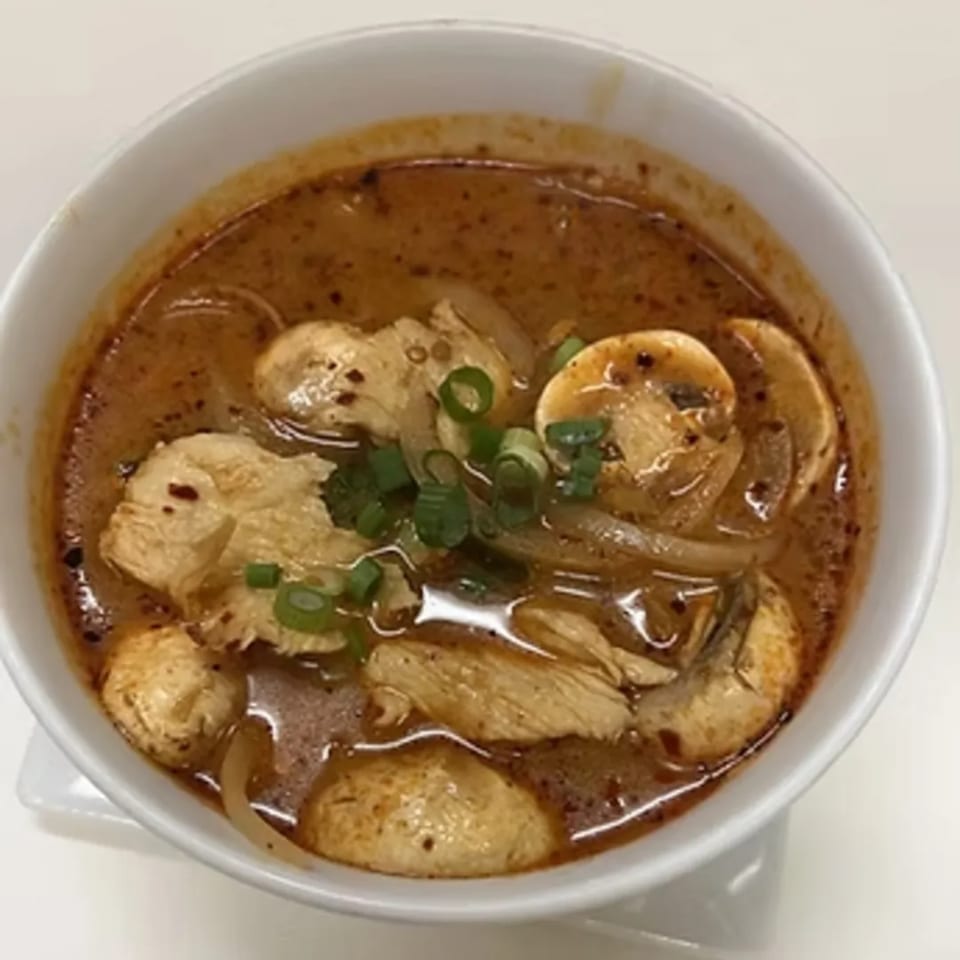 A bowl of Charm Thai Cuisine's Tom Yum soup with chicken, mushrooms, and green onions.