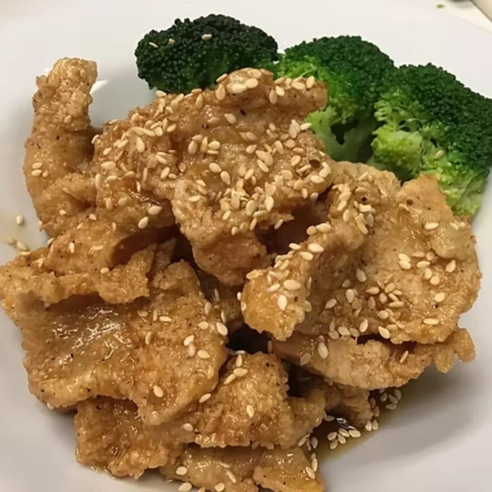 Sesame chicken with a side of steamed broccoli on a white plate from Charm Thai Cuisine.