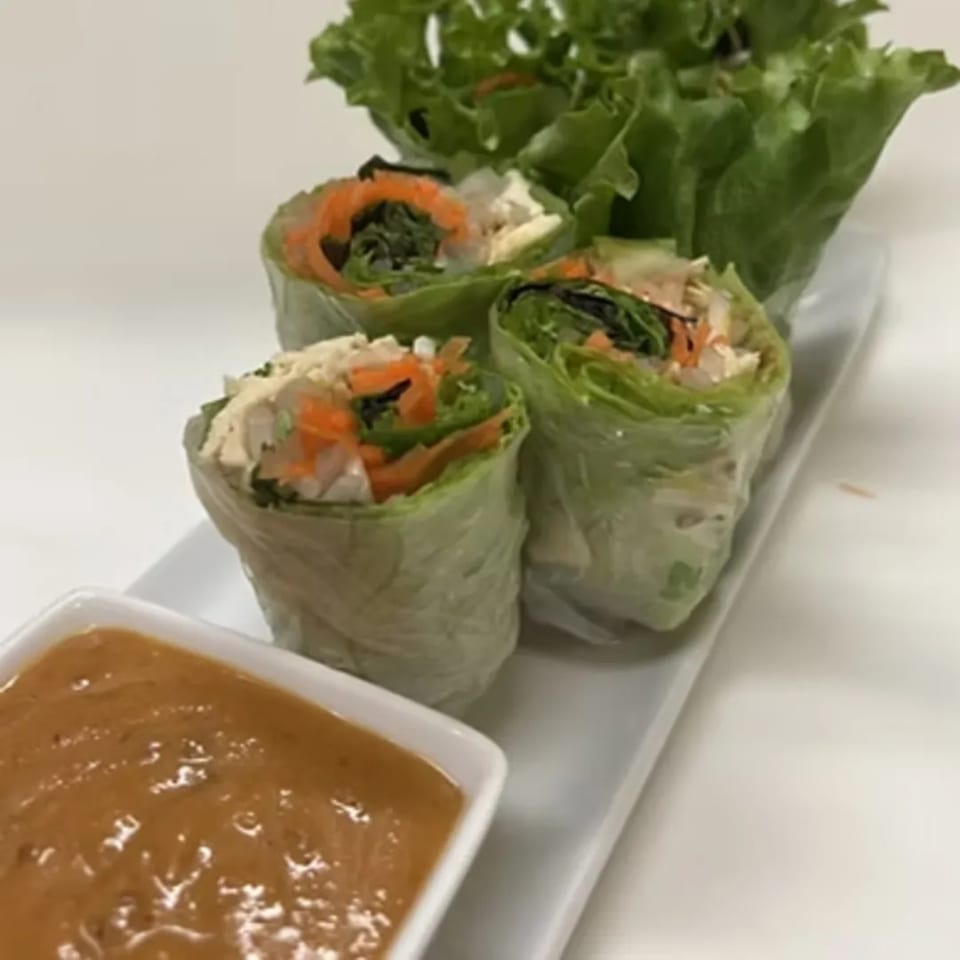 Fresh Thai spring rolls with lettuce, carrots, and chicken, served with a side of peanut sauce.
