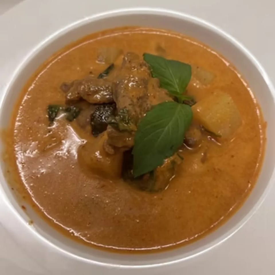 A bowl of Charm Thai Cuisine's red curry with chicken, potatoes, and basil leaves.