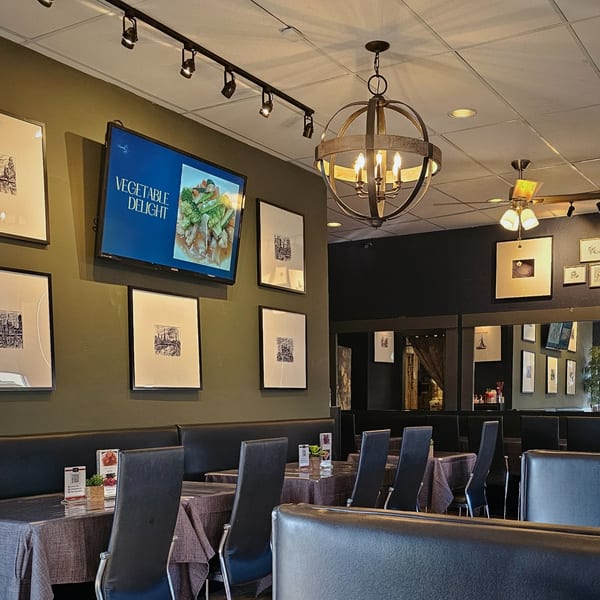 Interior of Charm Thai Cuisine with dark green walls, black booths, and a TV displaying "Vegetable Delight".