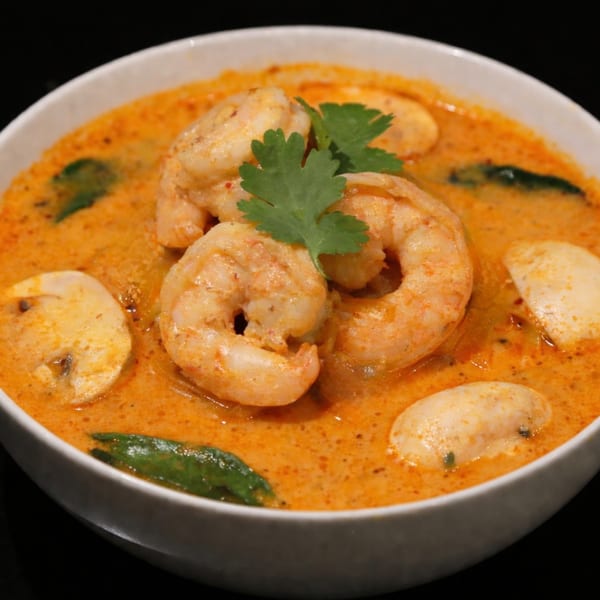 A close-up of Charm Thai Cuisine's Tom Yum Goong soup with shrimp, mushrooms, and cilantro.