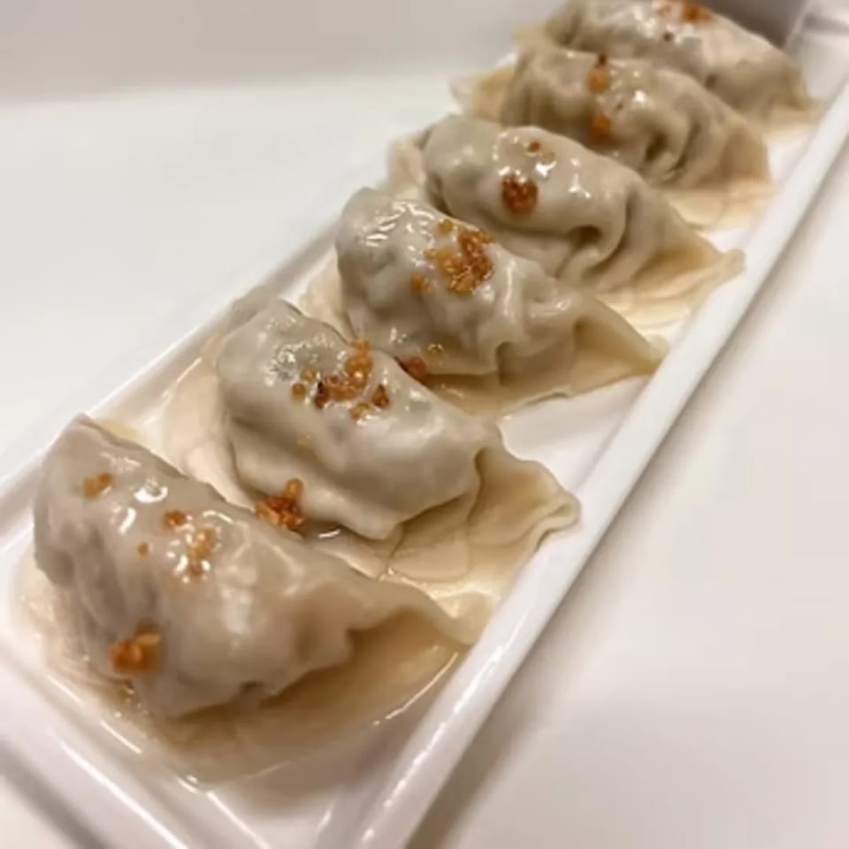 Five steamed dumplings with crispy garlic on a white rectangular plate, served at Charm Thai Cuisine.