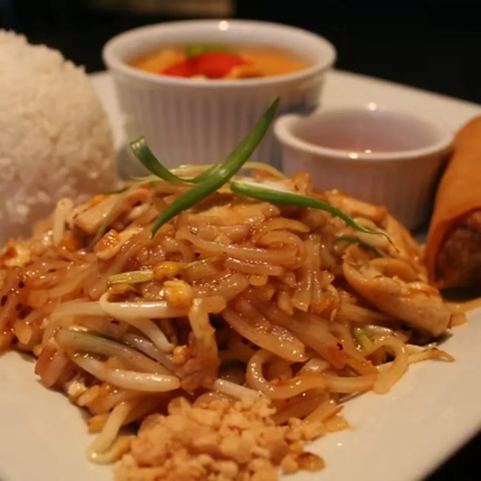 Charm Thai Cuisine's Pad Thai with rice, soup, and an egg roll on a white plate.