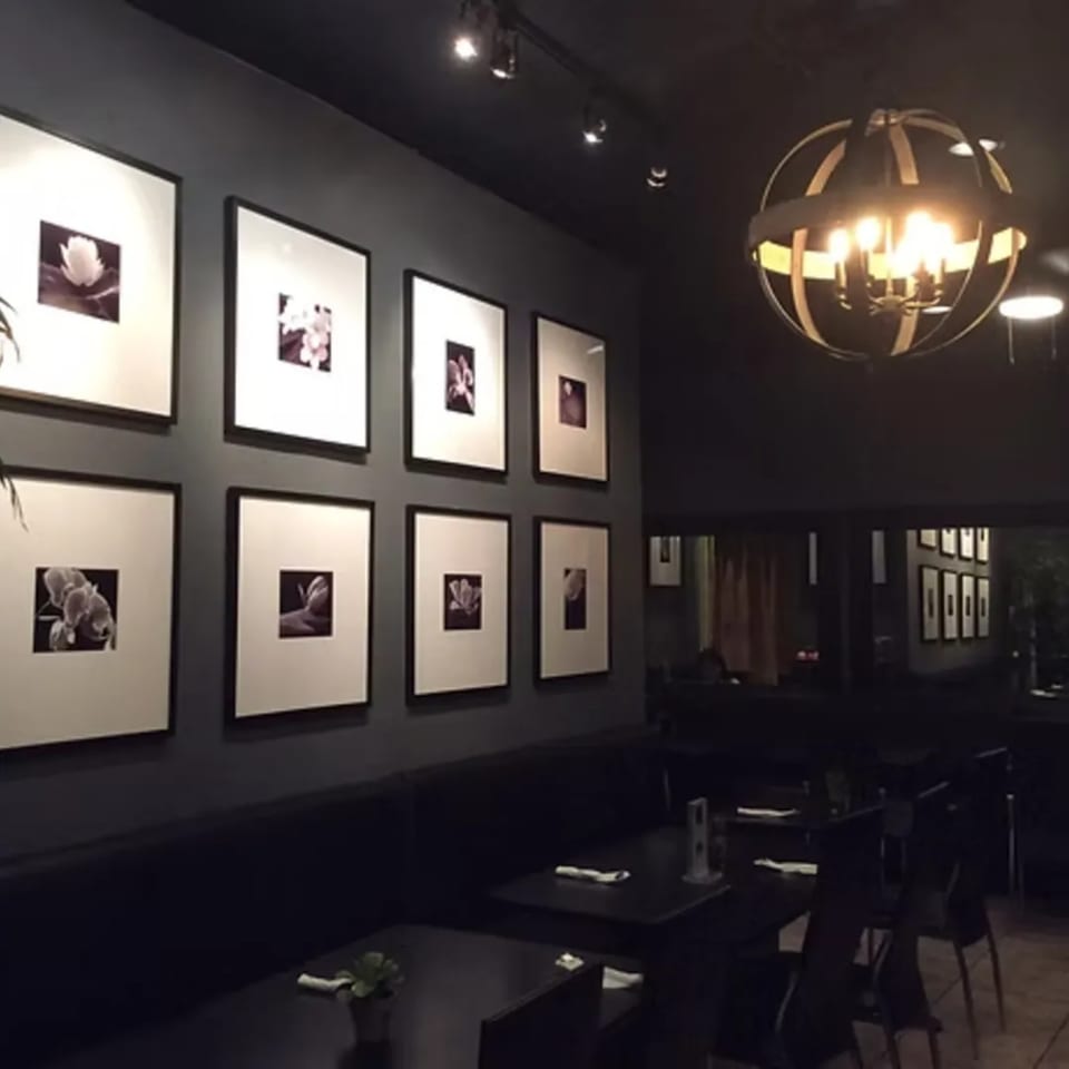 Dark, modern dining room at Charm Thai Cuisine with framed floral art, booth seating, and orb chandelier.