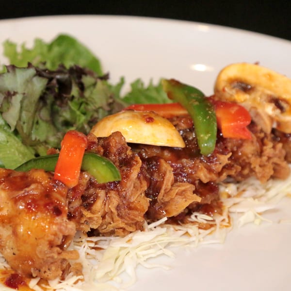 Crispy Thai chicken with bell peppers, mushrooms, and a side salad on a white plate.