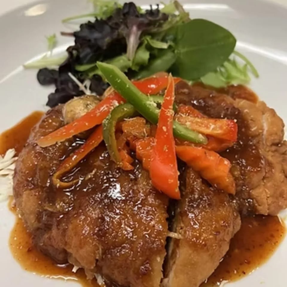Crispy duck with brown sauce, red and green bell peppers, and a side salad on a white plate.