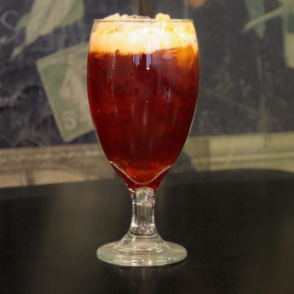 A tall glass of iced Thai tea with a creamy top layer, on a dark table.
