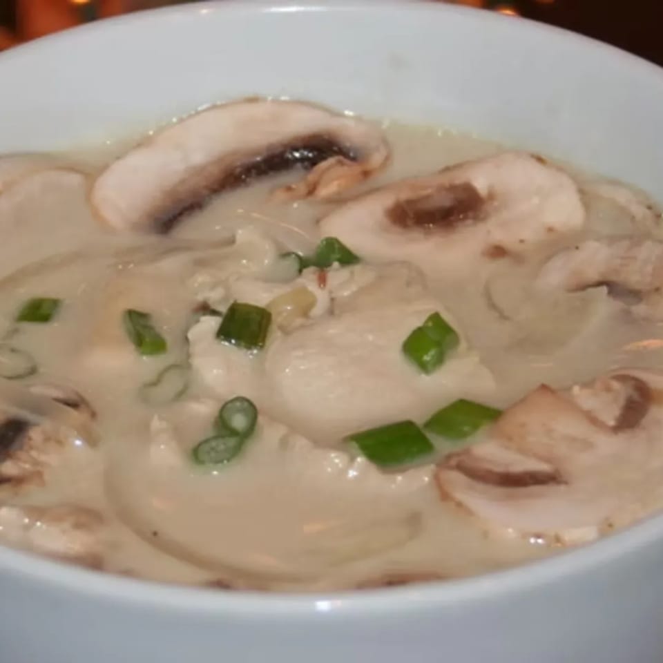 Close-up of a bowl of Charm Thai Cuisine's Tom Kha Gai soup with mushrooms, chicken, and green onions.