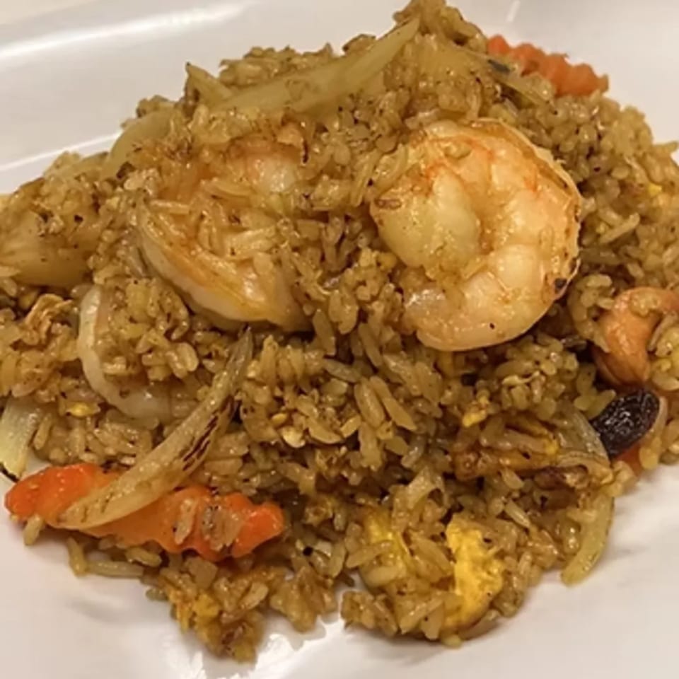 Close-up of Charm Thai Cuisine's shrimp fried rice with onions, carrots, and cashews on a white plate.