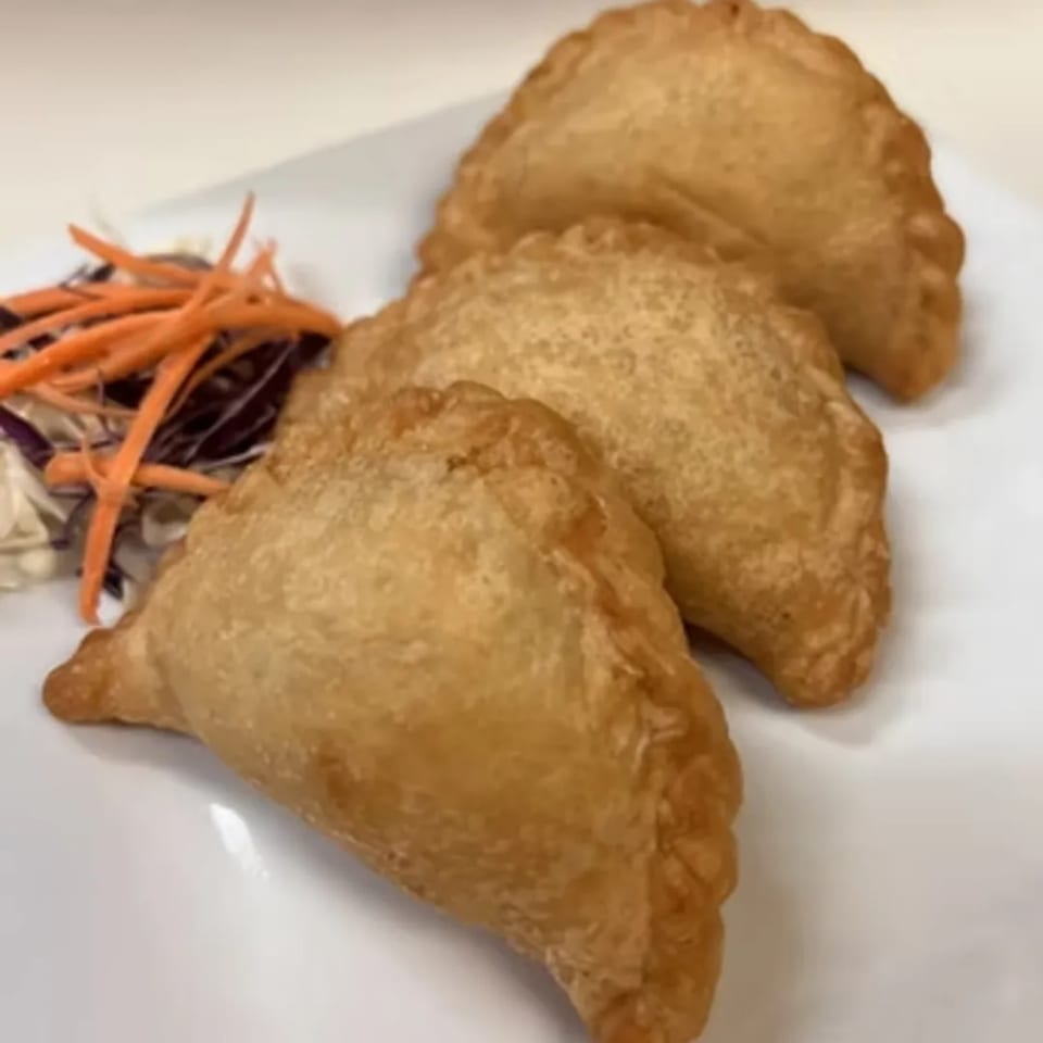 Three golden-brown Thai curry puffs with crimped edges, served with shredded carrots and cabbage.