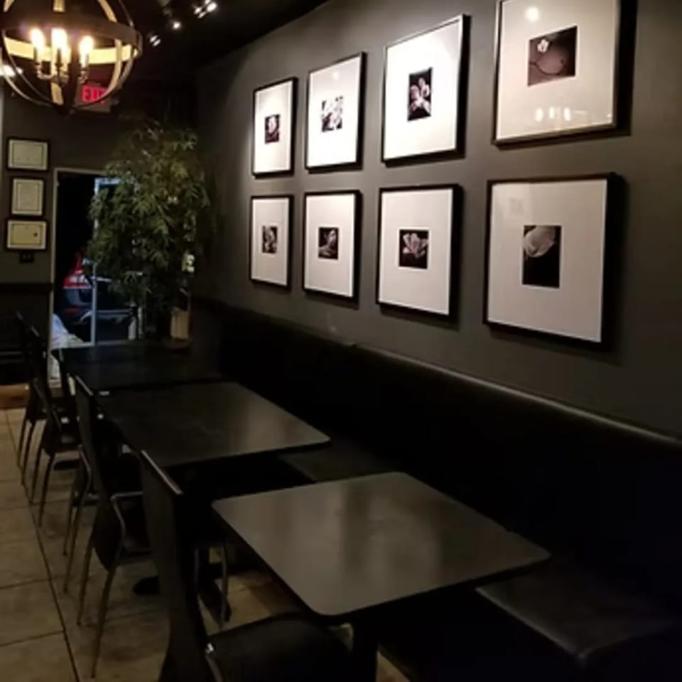 Interior of Charm Thai Cuisine with dark tables, chairs, banquette seating, and framed artwork on the wall.
