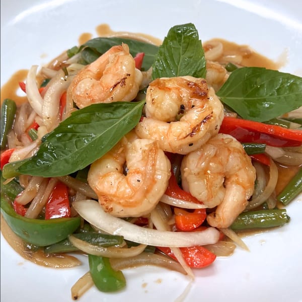 Close-up of Charm Thai Cuisine's shrimp stir-fry with onions, peppers, and basil on a white plate.