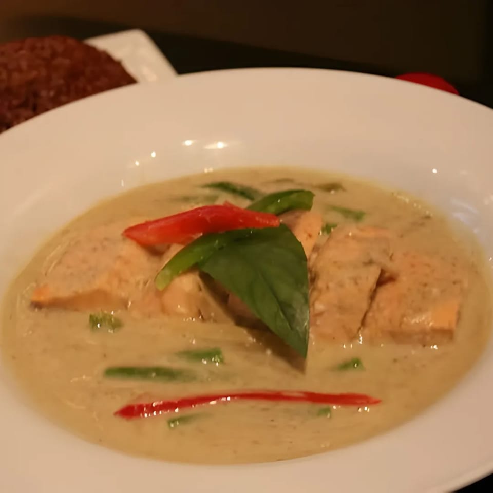 Charm Thai Cuisine's green curry with salmon, green beans, red peppers, and basil in a white bowl.