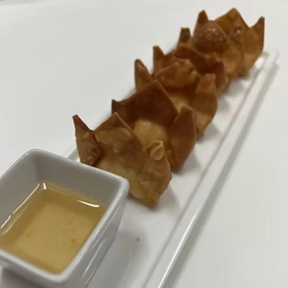 Crispy golden crab rangoons with a side of sweet and sour dipping sauce on a white plate.