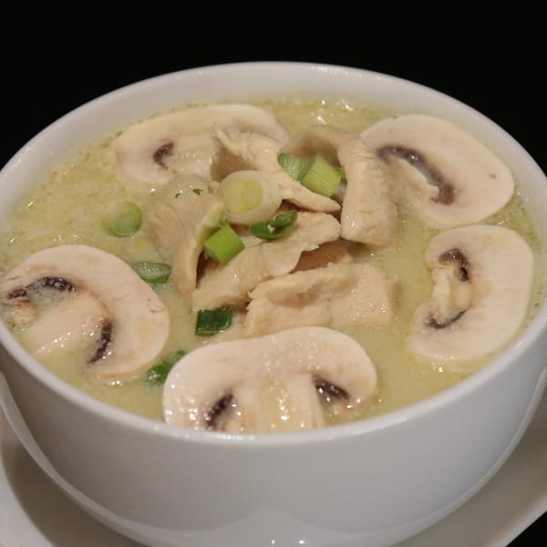 Charm Thai Cuisine's Tom Kha Gai soup with chicken, mushrooms, and green onions in a white bowl.